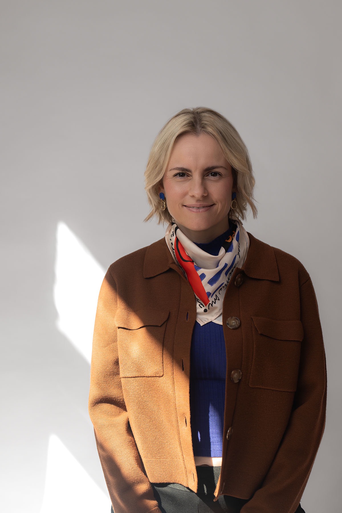 Judith Storm steht vor einer hellen Wand, mit buntem Seidentuch und braunem Blazer.
