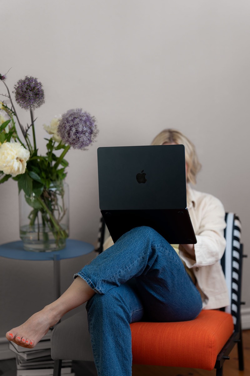 Judith Storm auf einem orangefarbenen Sessel, das Gesicht hinter einem aufgeklappten Laptop verborgen.