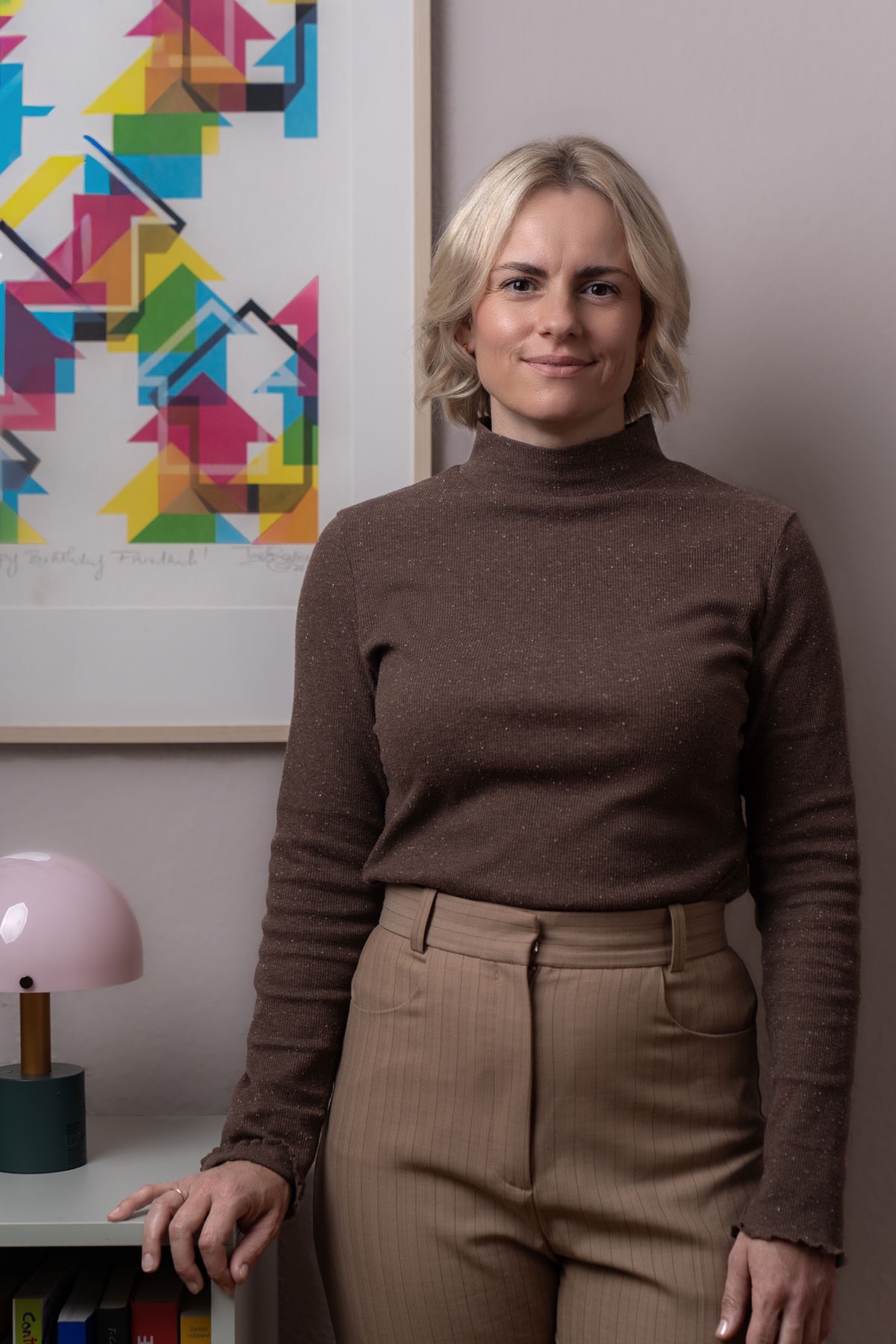 Judith Storm lehnt in ihrer Praxis an einem Regal vor einem bunten Kunstdruck.