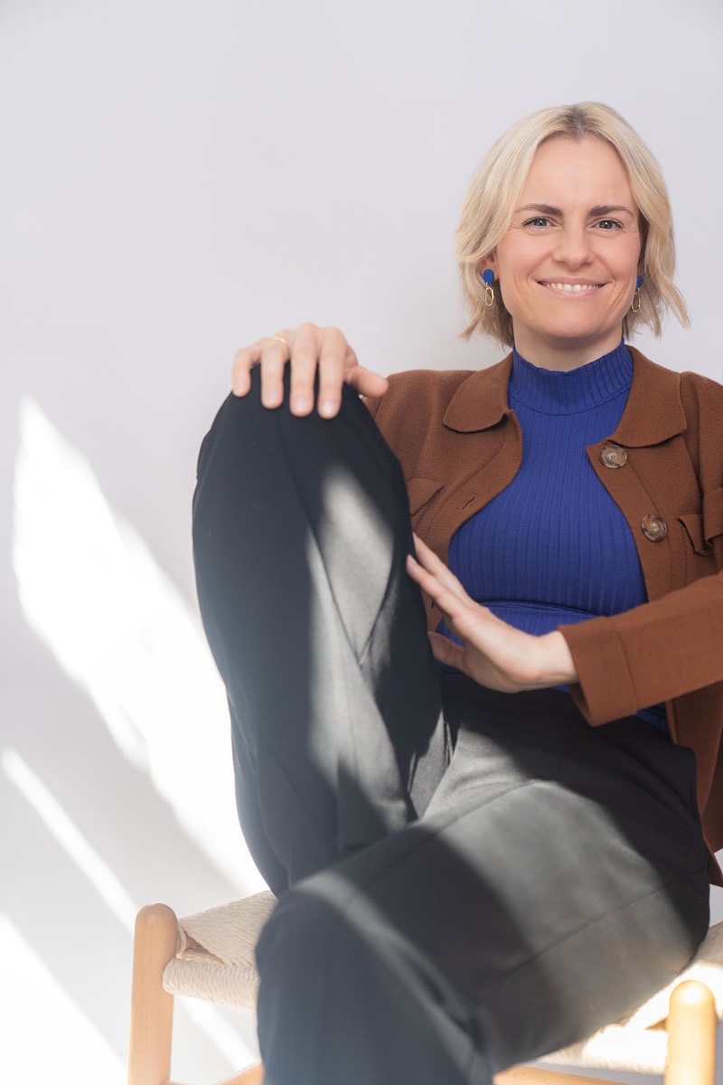 Judith Storm lacht in die Kamera, ein Knie angezogen.