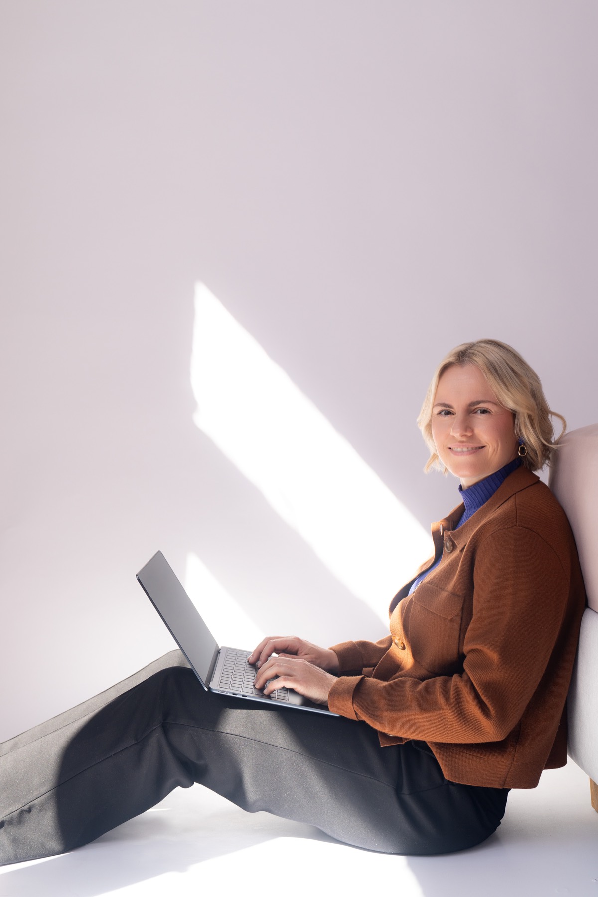 Judith Storm sitzt mit Laptop im Sonnenlicht auf dem Boden und lächelt in die Kamera.