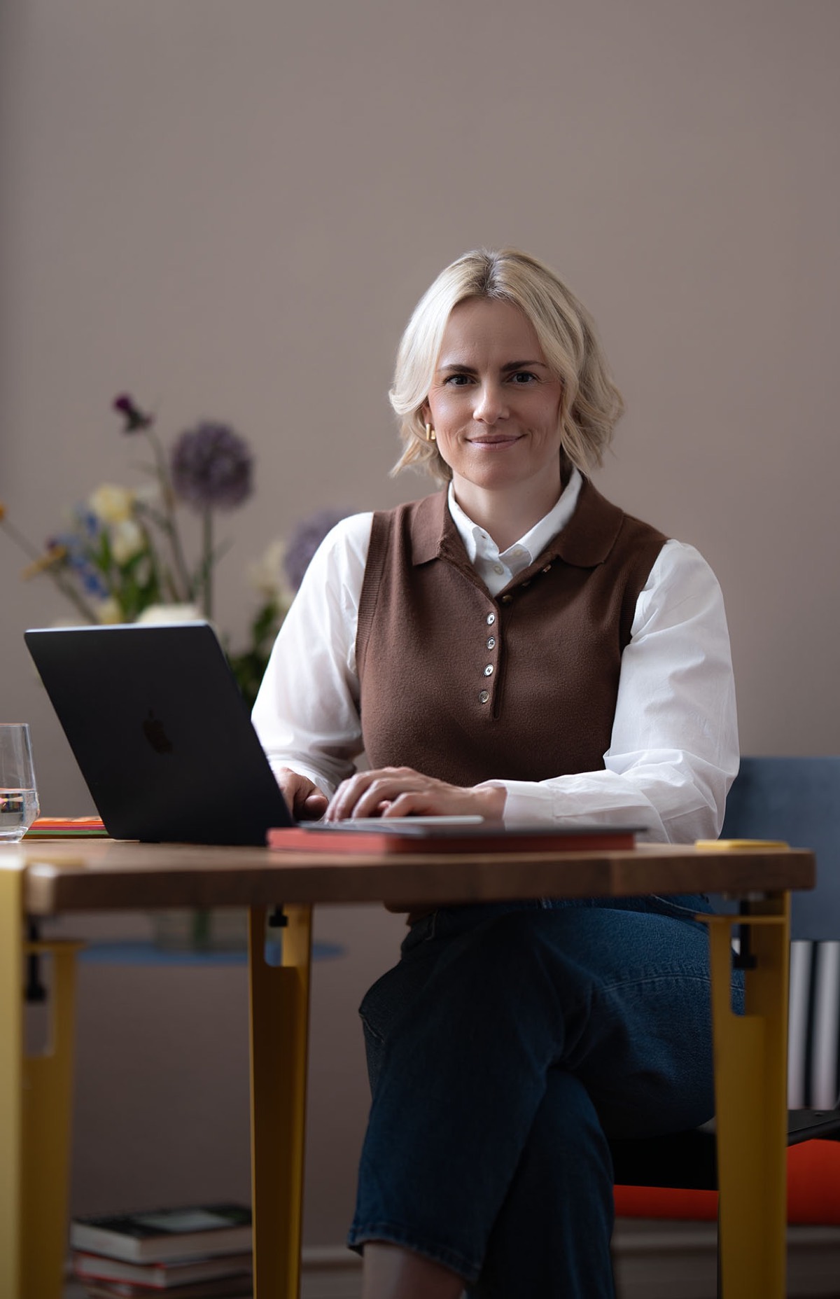 Judith Storm sitzt am Schreibtisch mit Laptop, daneben Blumen.